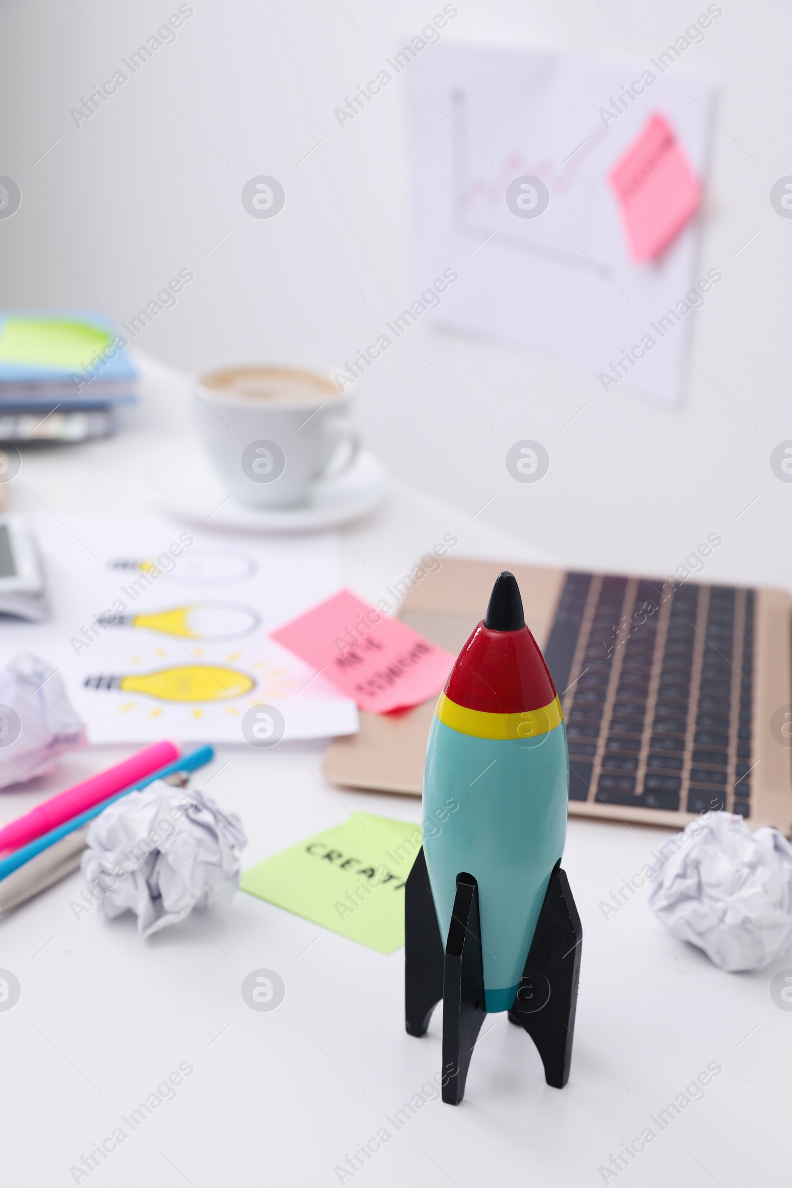 Photo of Toy rocket, laptop and crumpled paper on messy table indoors. Startup concept