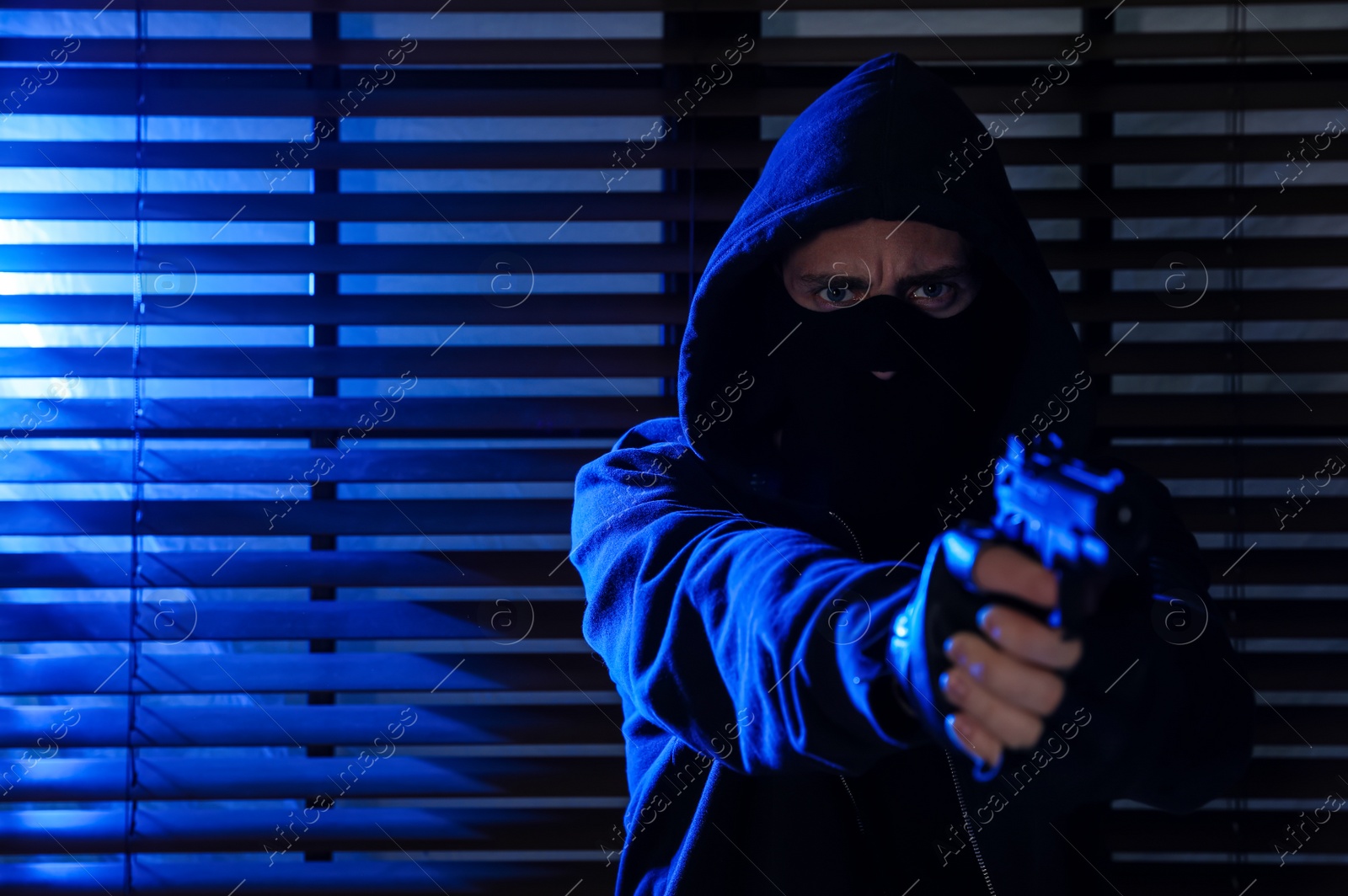 Photo of Man in mask with gun near window indoors. Dangerous criminal