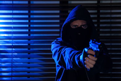 Man in mask with gun near window indoors. Dangerous criminal