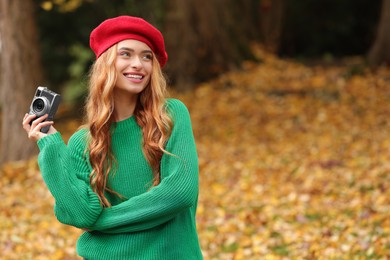 Photo of Smiling woman with camera in autumn park. Space for text
