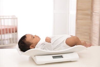 African-American baby lying on scales in light room