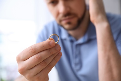 Photo of Man holding wedding ring on light background, closeup. Divorce concept