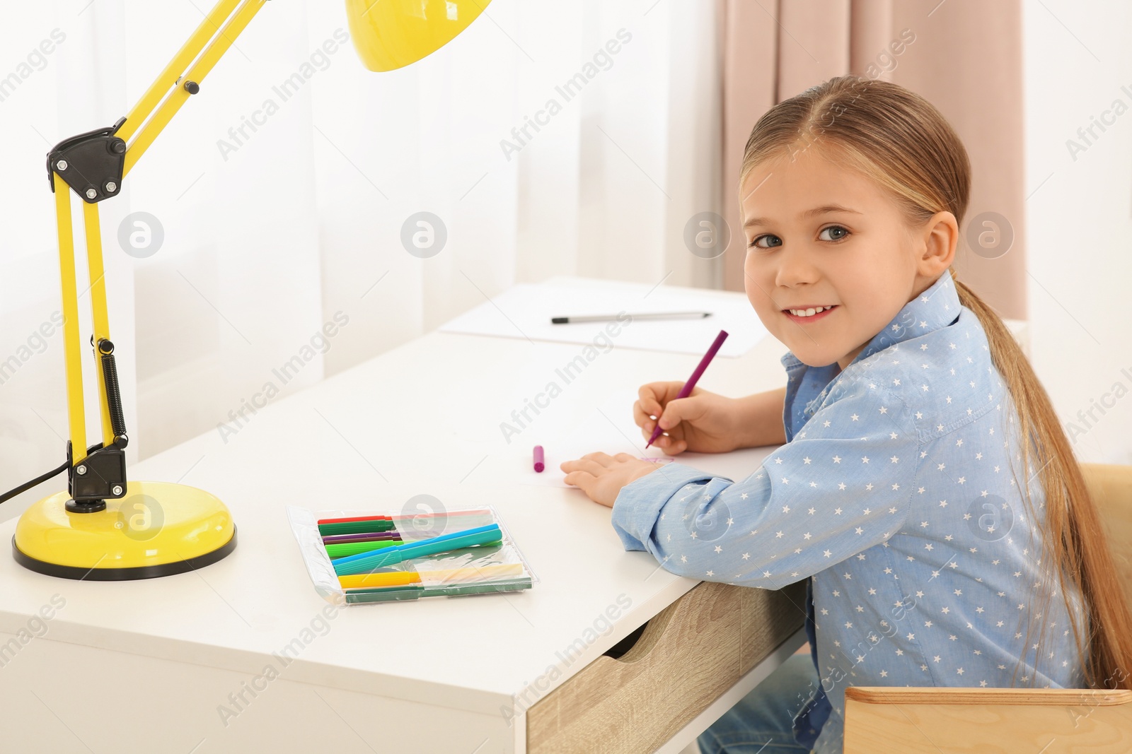 Photo of Cute little girl drawing with marker at desk in room. Home workplace