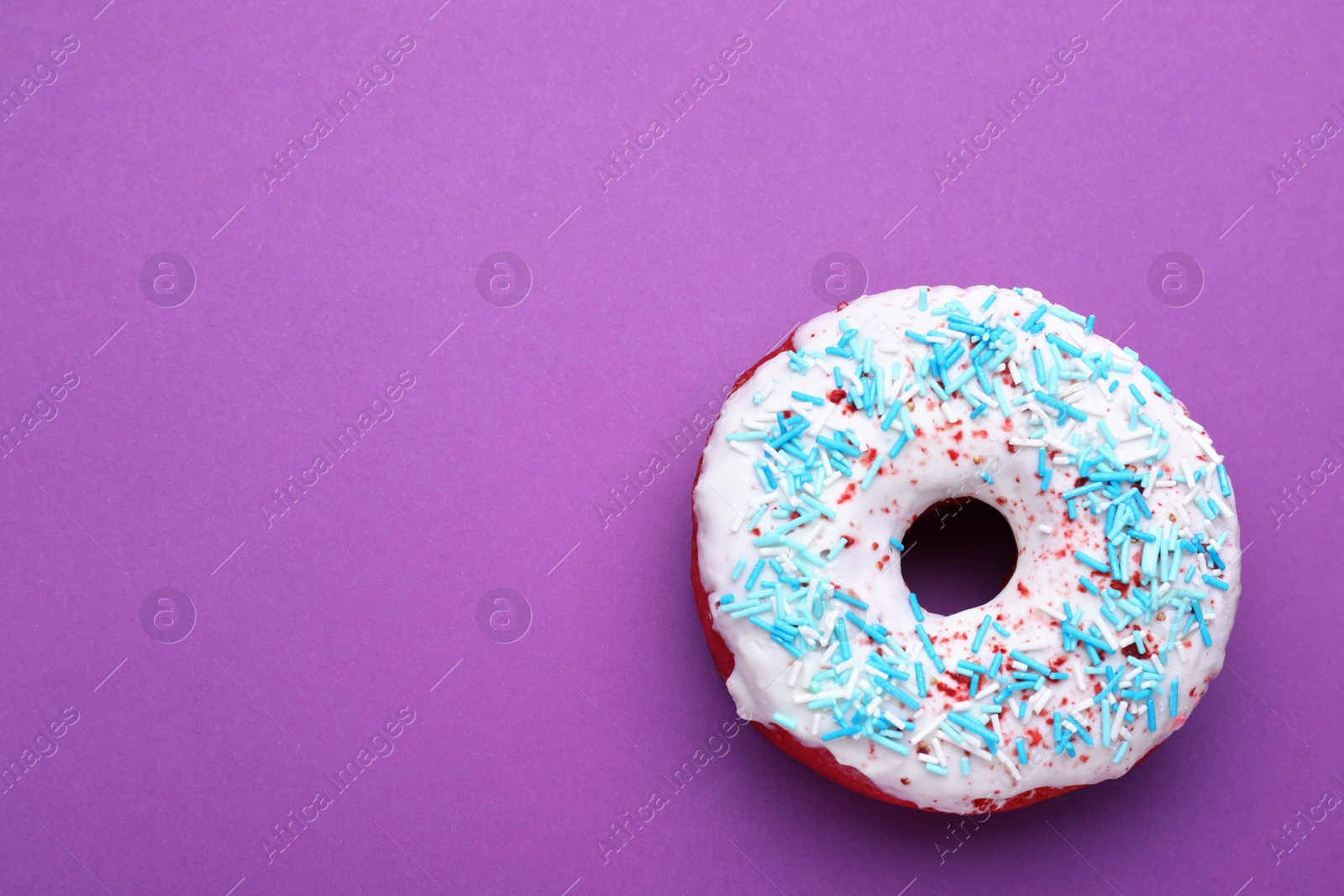 Photo of Sweet glazed donut decorated with sprinkles on purple background, top view and space for text. Tasty confectionery