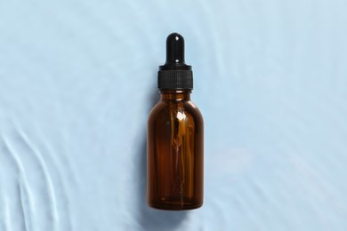 Photo of Bottle of cosmetic serum and water on light blue background, top view