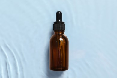 Bottle of cosmetic serum and water on light blue background, top view