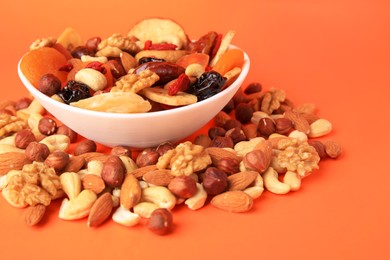 Bowl and mixed dried fruits with nuts on orange background, closeup