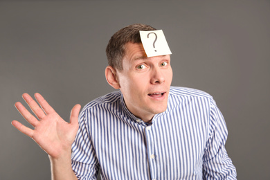 Emotional man with question mark on grey background