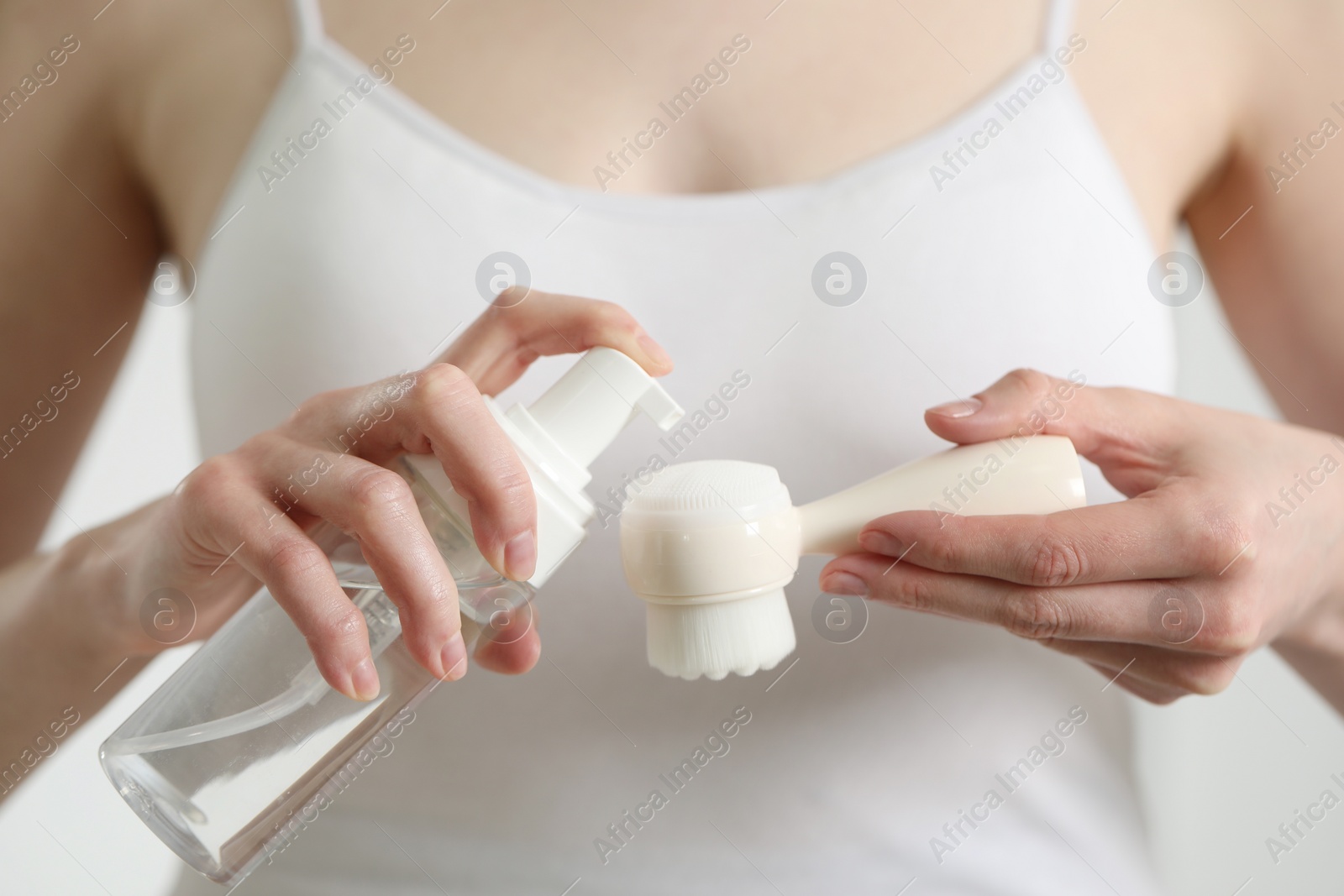 Photo of Washing face. Woman applying cleansing foam onto brush against light background, closeup