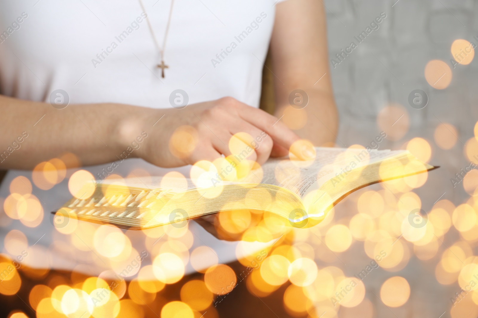 Image of Woman reading Bible near white wall, closeup. Bokeh effect