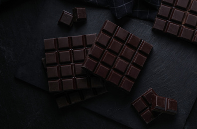 Photo of Tasty dark chocolate bars on black table, flat lay