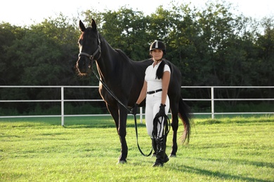 Young woman in horse riding suit and her beautiful pet outdoors on sunny day