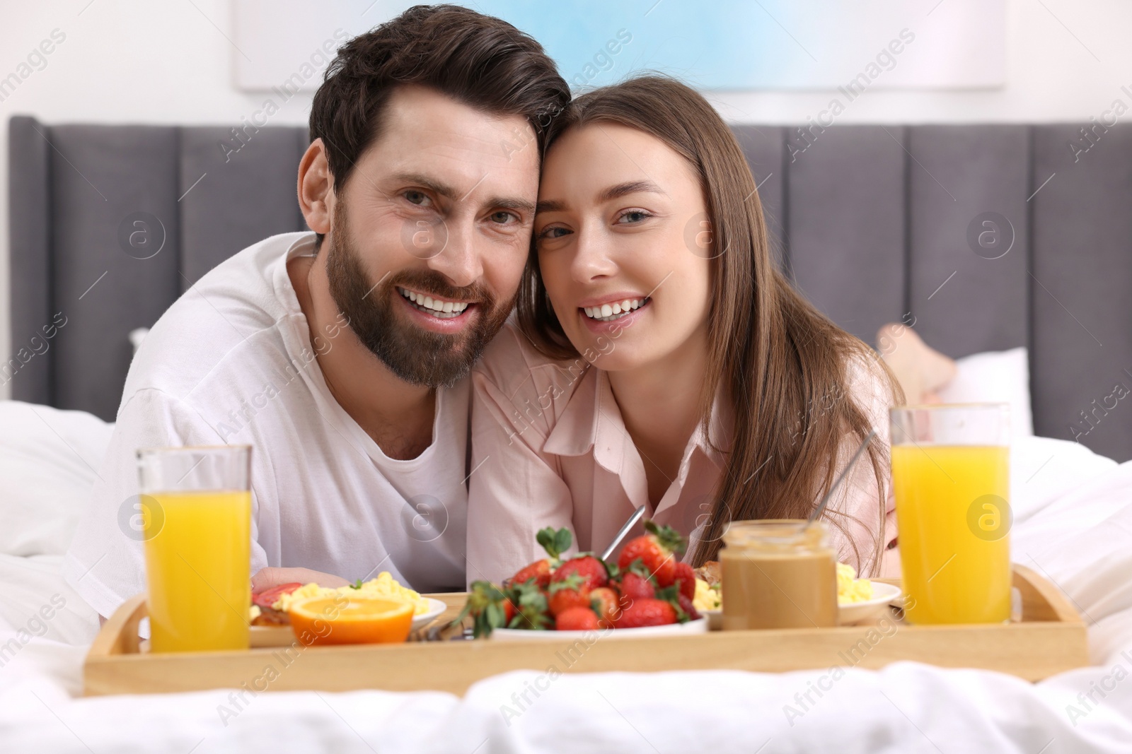 Photo of Family portrait of happy couple with tray of tasty breakfast on bed at home