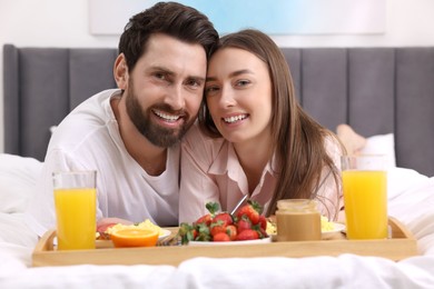 Photo of Family portrait of happy couple with tray of tasty breakfast on bed at home