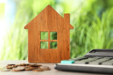 Photo of Wooden house model, calculator and coins on table outdoors