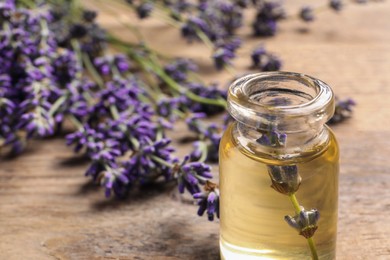 Photo of Bottle of essential oil and lavender flowers on wooden table, closeup. Space for text