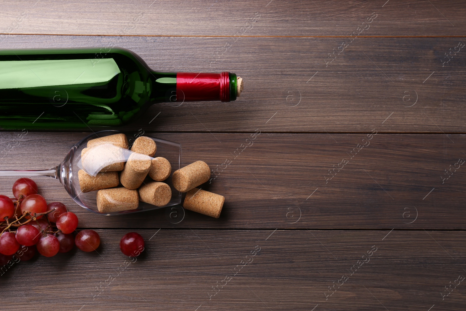 Photo of Bottle of wine, glass with corks and grapes on wooden table, flat lay. Space for text