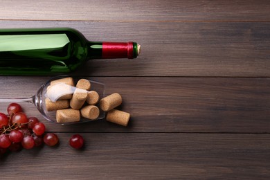 Photo of Bottle of wine, glass with corks and grapes on wooden table, flat lay. Space for text