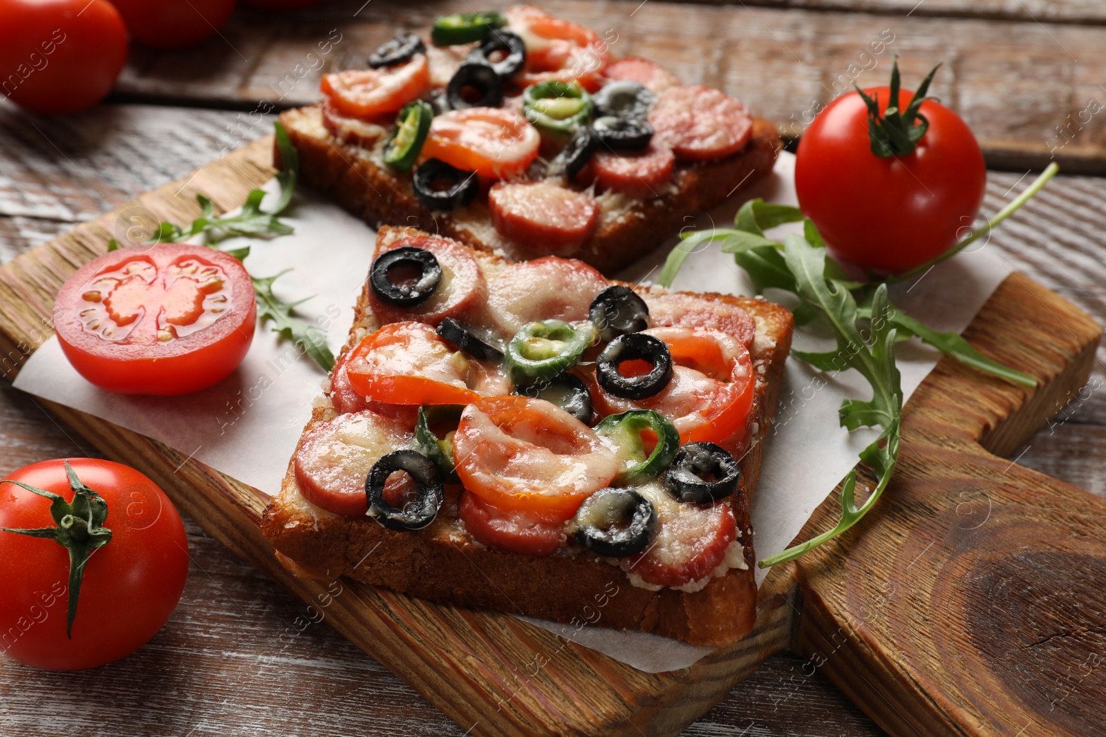 Photo of Tasty pizza toasts, tomatoes and arugula on wooden table, closeup