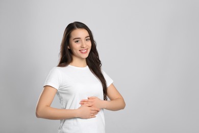 Photo of Happy healthy woman touching her belly on light grey background, space for text