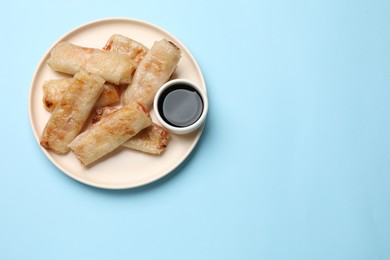 Photo of Fried spring rolls and sauce on light blue table, top view. Space for text