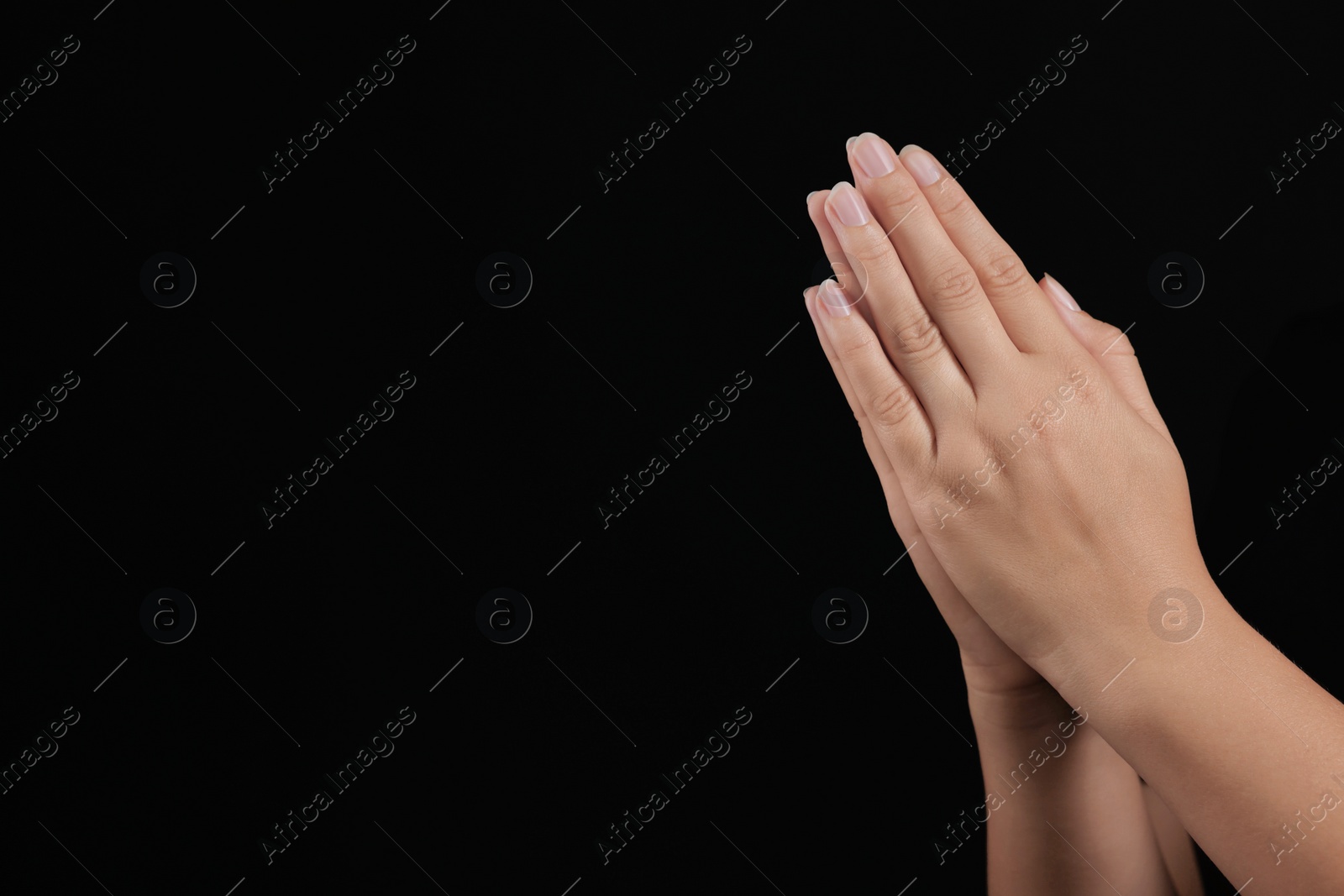 Photo of Woman holding hands clasped while praying against black background, closeup. Space for text