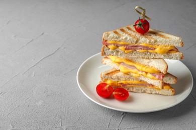 Photo of Stack of tasty sandwiches with ham and melted cheese served with tomatoes on grey textured table, space for text