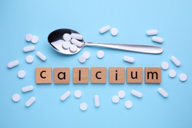 Photo of Word Calcium made of wooden cubes with letters, spoon and pills on turquoise background, flat lay
