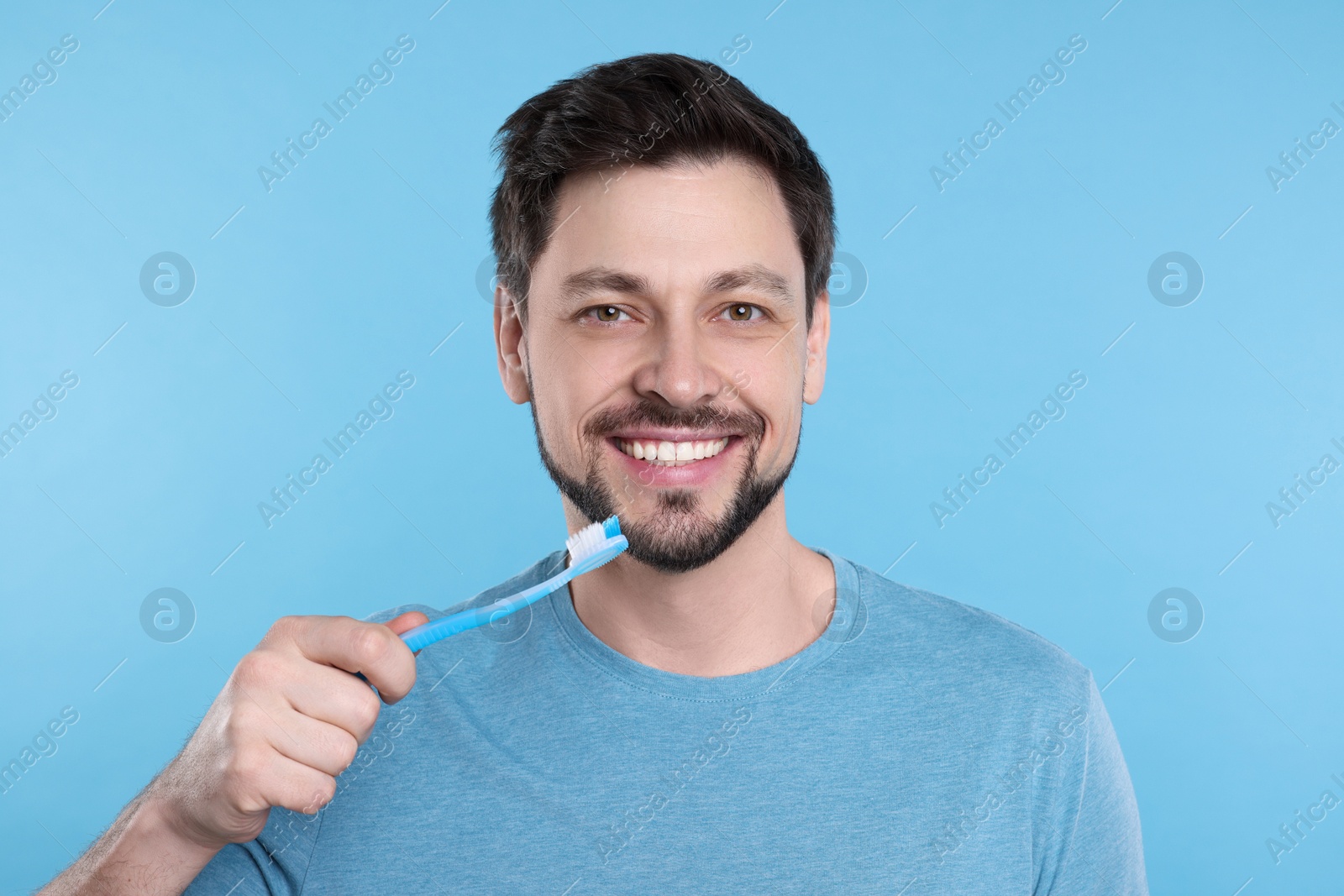 Photo of Happy man holding plastic toothbrush on light blue background