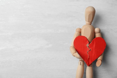 Photo of Wooden puppet holding torn cardboard heart on gray background, top view with space for text. Relationship problems