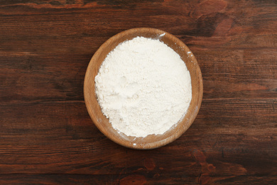 Photo of Bowl with flour on wooden table, top view