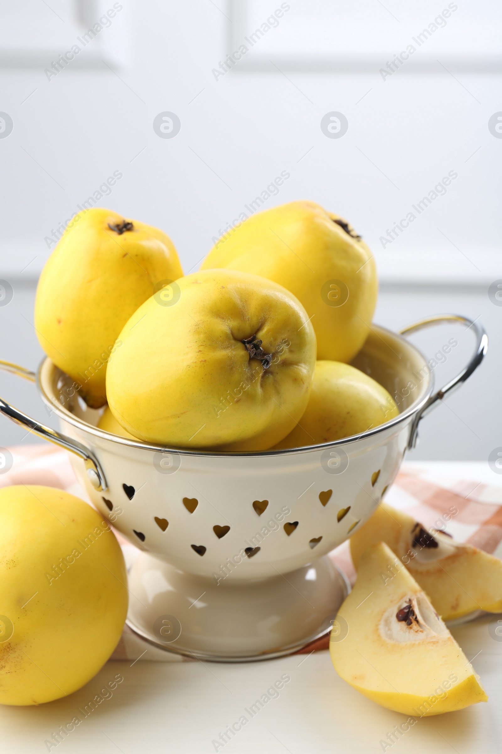 Photo of Tasty ripe quinces and metal colander on white wooden table