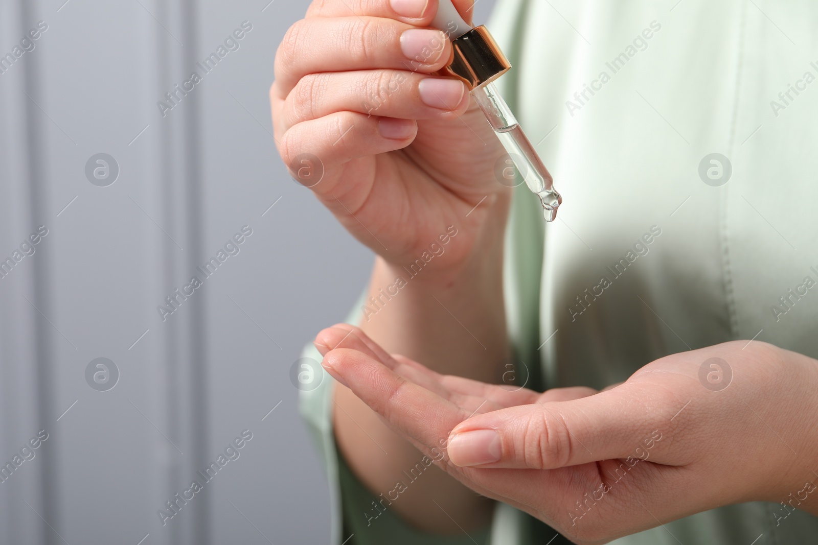 Photo of Woman applying cosmetic serum onto hand on grey background, closeup. Space for text