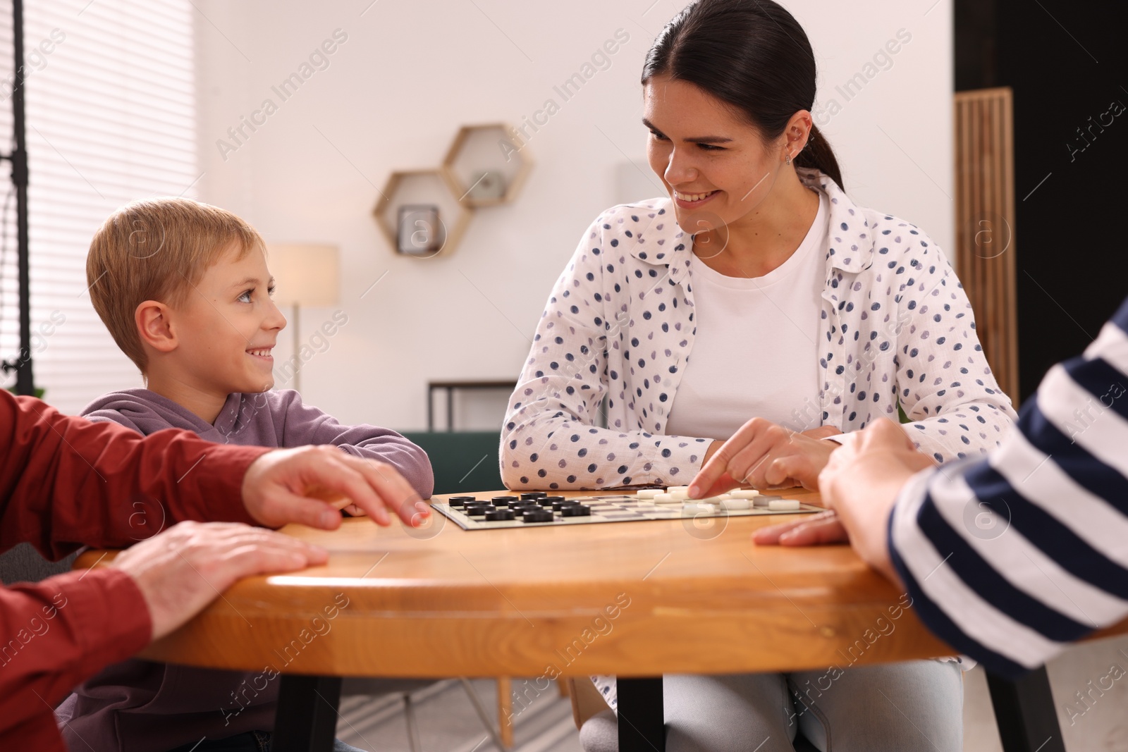 Photo of Family playing checkers at wooden table in room