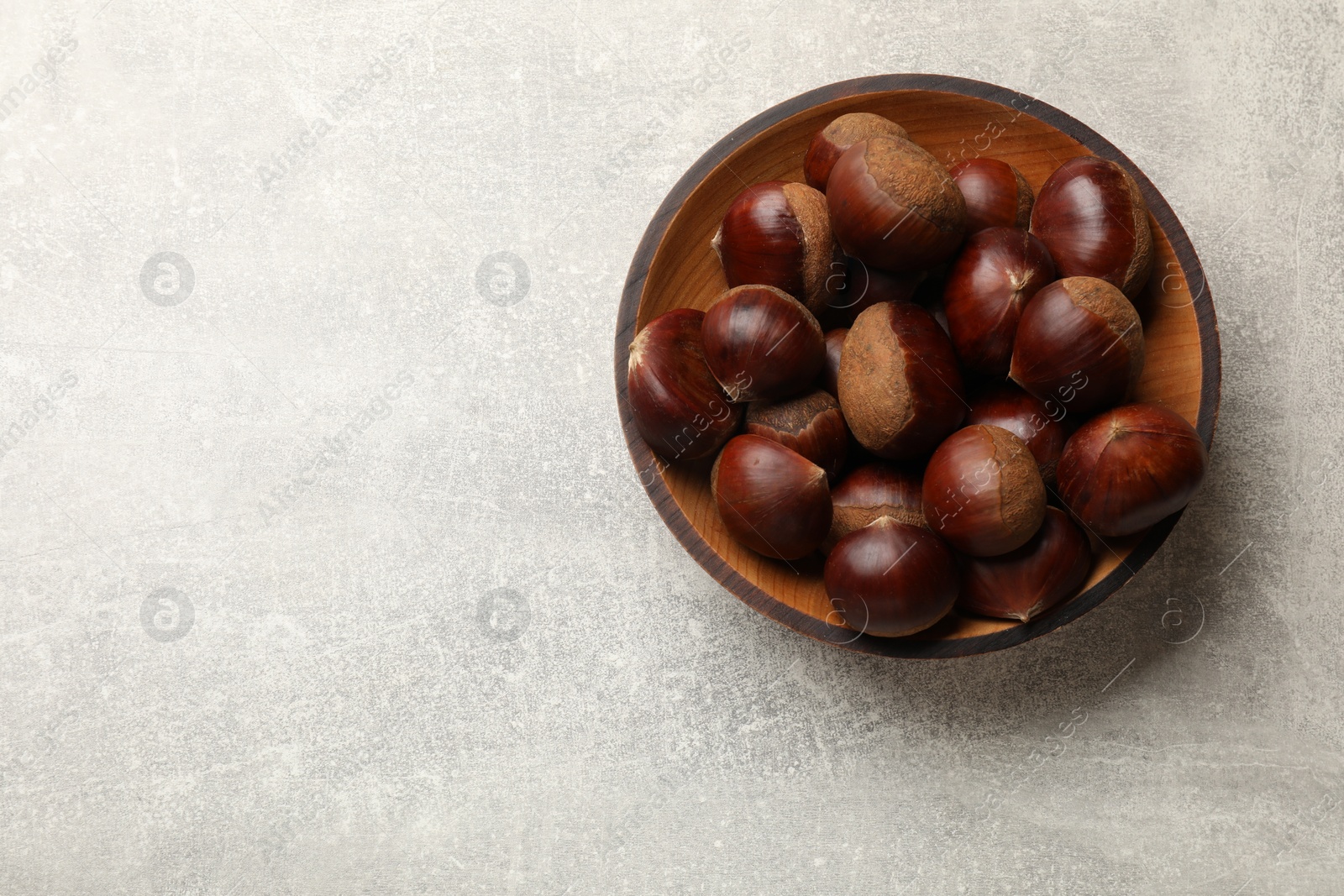 Photo of Roasted edible sweet chestnuts in bowl on light grey table, top view. Space for text