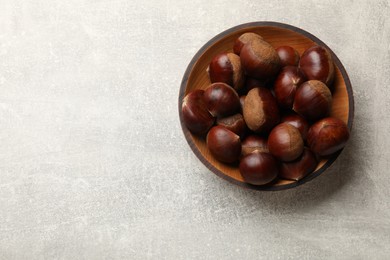 Roasted edible sweet chestnuts in bowl on light grey table, top view. Space for text