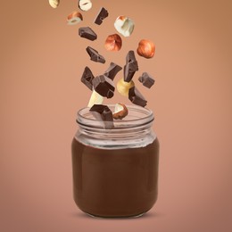 Image of Making yummy chocolate paste. Hazelnuts and pieces of chocolate falling into jar on light brown background