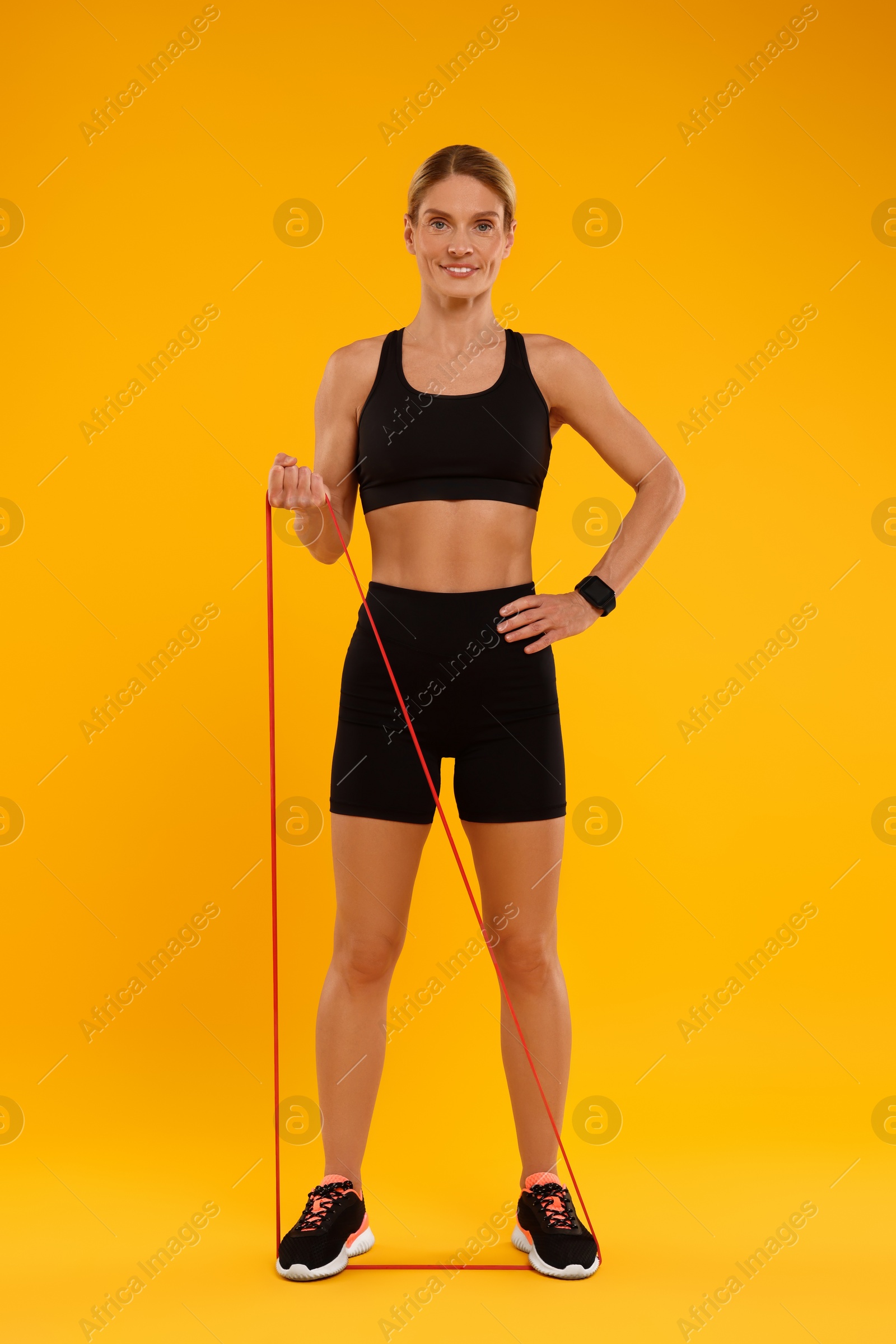 Photo of Woman exercising with elastic resistance band on orange background