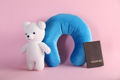 Photo of Light blue travel pillow, toy bear and passport on pink background