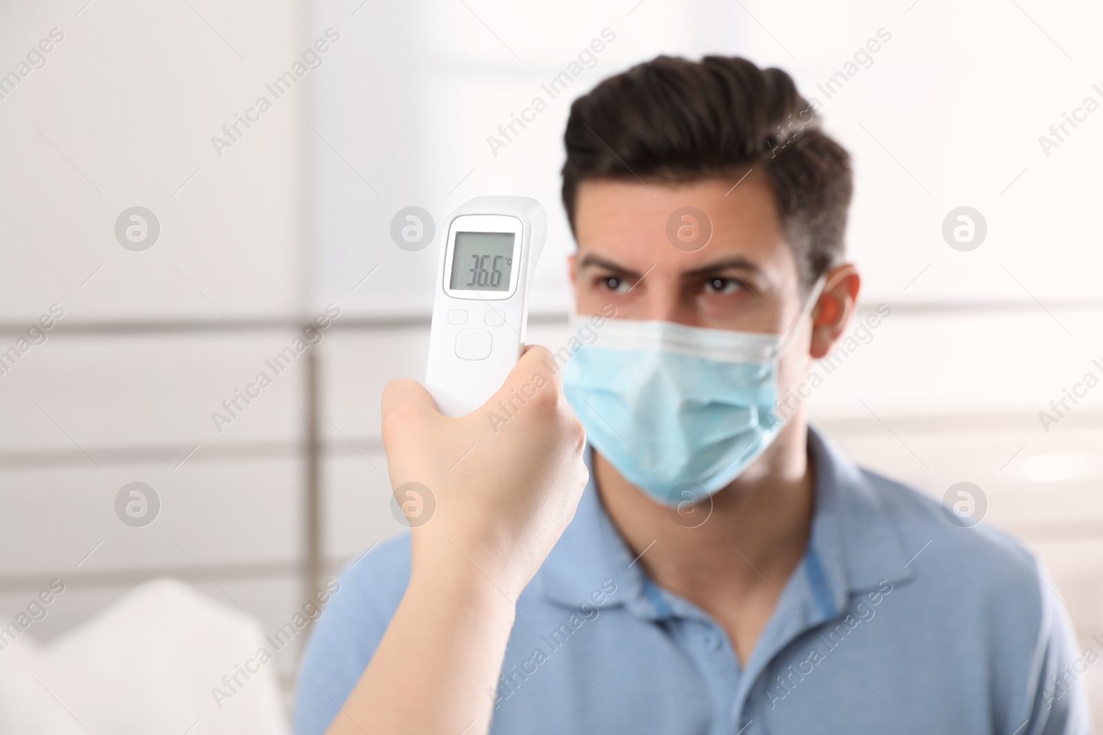 Photo of Doctor measuring man's temperature indoors, closeup. Prevent spreading of Covid-19