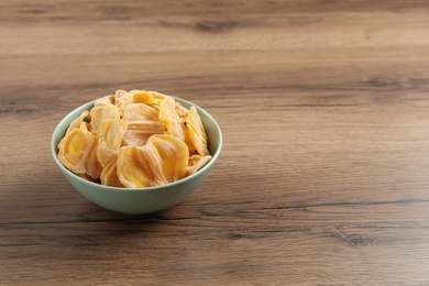 Delicious dried jackfruit slices in bowl on wooden table. Space for text