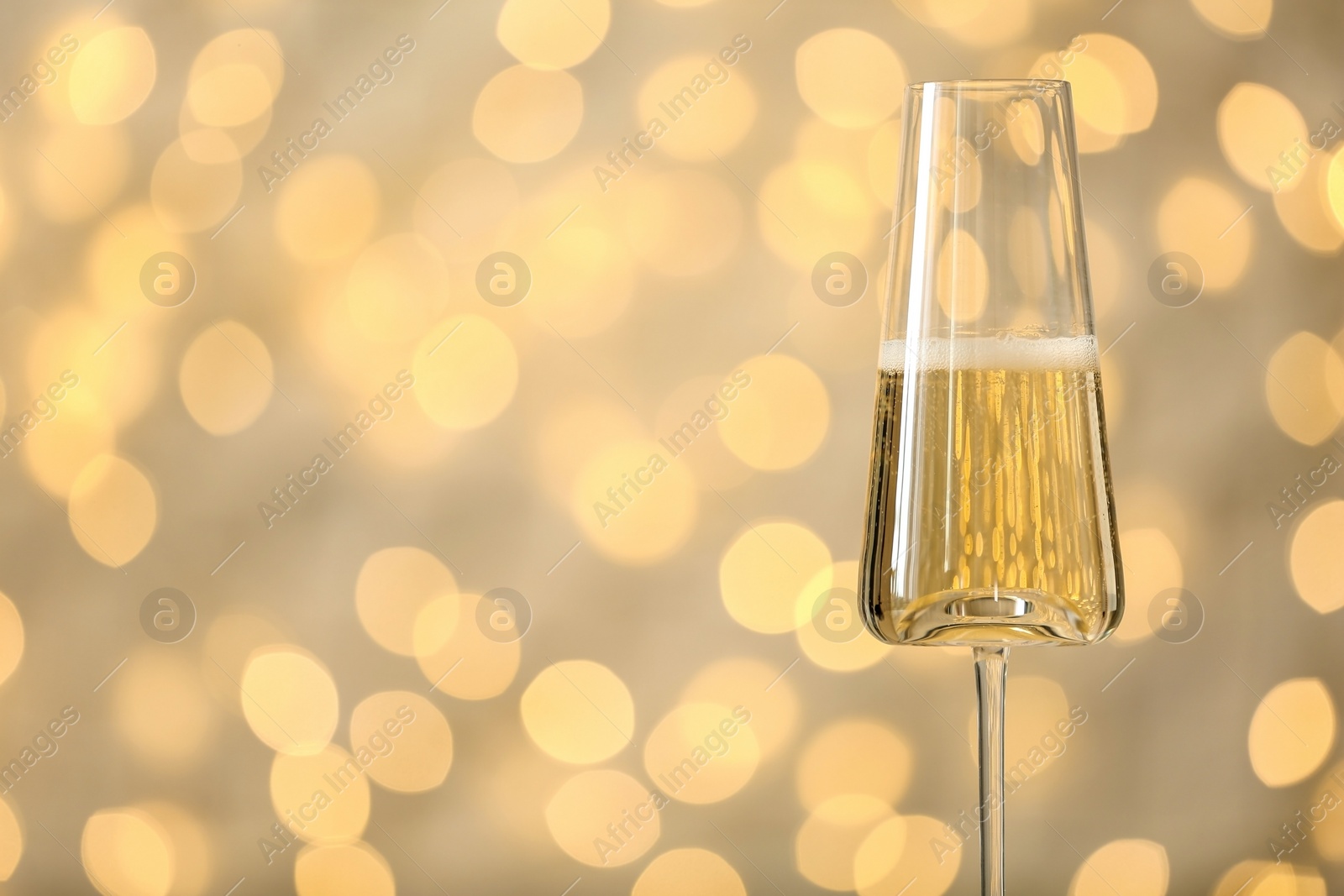 Photo of Glass of fizzy champagne against blurred fairy lights, space for text