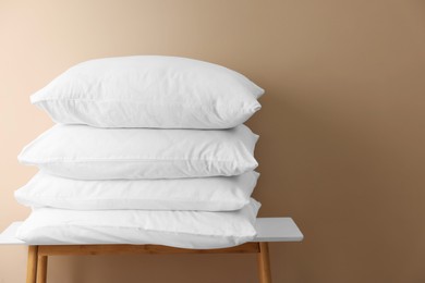 Stack of soft white pillows on table near beige wall. Space for text
