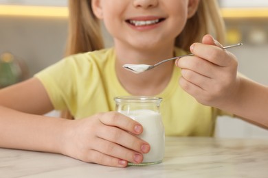 Photo of Cute little girl with tasty yogurt at white marble table indoors, closeup