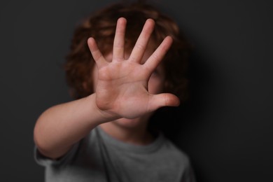 Child abuse. Boy making stop gesture near grey wall, selective focus
