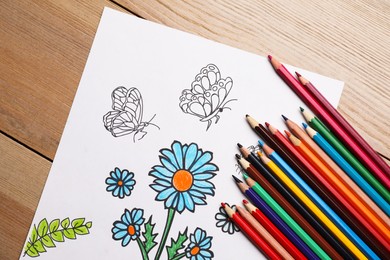 Photo of Child's colored drawing with pencils on wooden table, flat lay