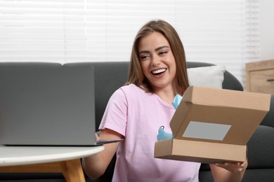 Photo of Happy woman using laptop while unpacking parcel at home. Online store