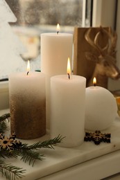 Photo of Beautiful burning candles with Christmas decor on windowsill indoors