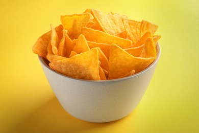 Photo of Tortilla chips (nachos) in bowl on yellow background, closeup