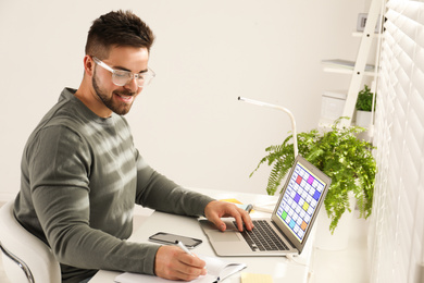 Photo of Young man using calendar app on laptop in office